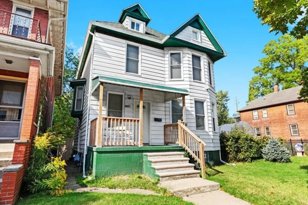 Two-story Victorian house with white siding, green roof trim, front porch, and wooden steps on residential street